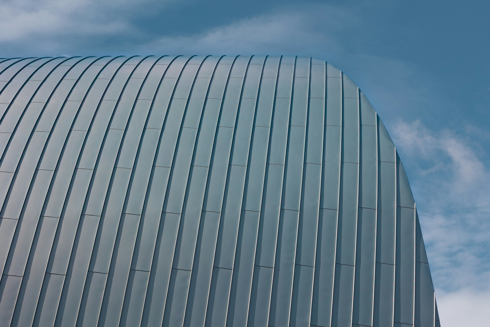 Curved metal structure against a cloudy blue sky.